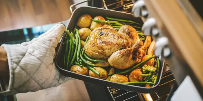 cook taking ready fried baked chicken with vegetables from the oven healthy cooking concept
