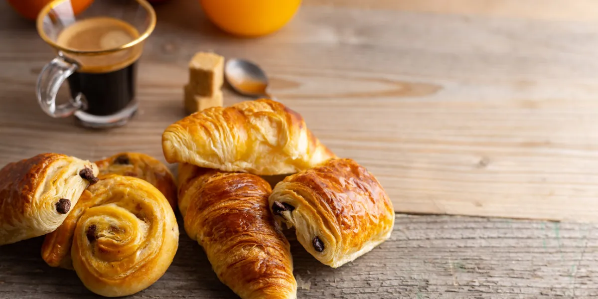 breakfast with croissants, cinnamon buns and chocolate cookies, fresh orange juice and coffee on the side on a wooden background