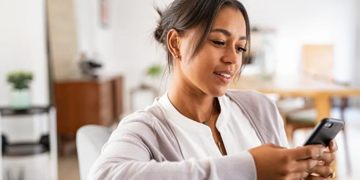 mature african woman sitting on couch at home using smartphone black woman relaxing on the sofa while messaging with a cellphone at home happy mature indian woman typing on mobile phone in living room