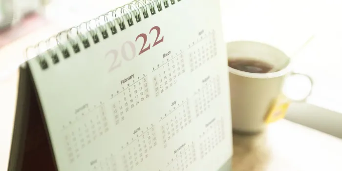 paper desktop calendar 2022 schedule with tea cup on wooden desk
