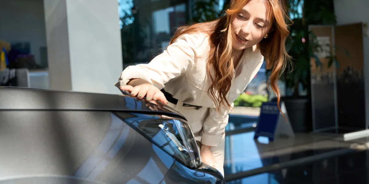 focused young auto dealership female customer running her hand over car hood