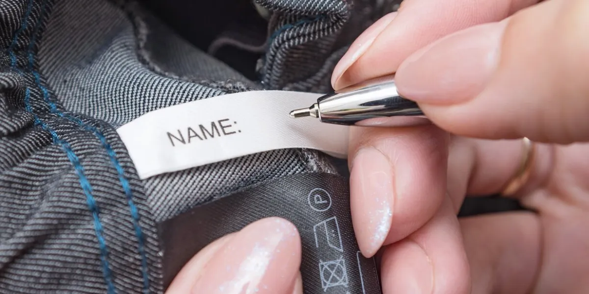 pen in mother's hands for fills the name label on children's school clothes child name, concept