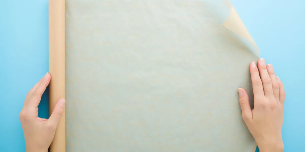 young adult woman hands using roll of baking paper on light blue table background pastel color closeup point of view shot top down view