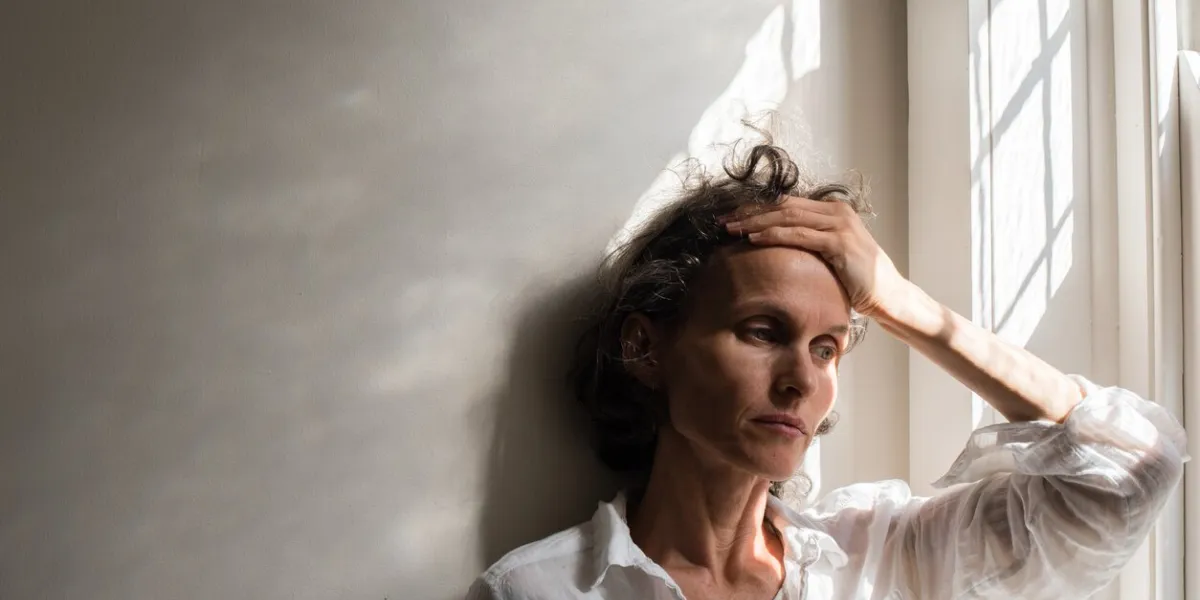thoughtful tensed woman against wall by window at home