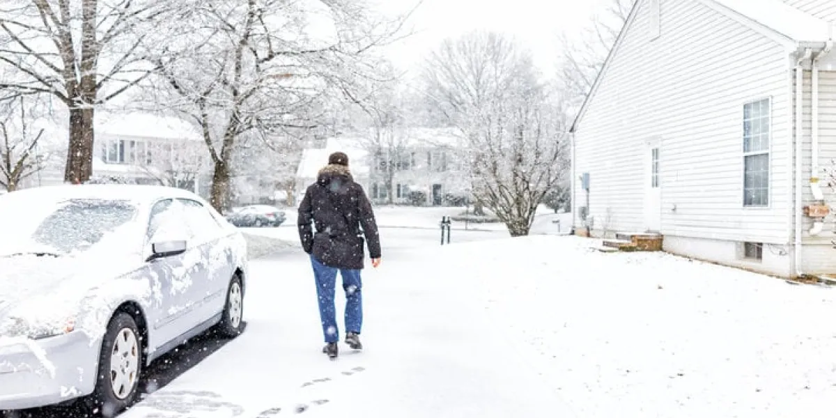 young man walking by car in driveway in neighborhood with snow covered ground during blizzard white storm, snowflakes falling in virginia suburbs, single family homes to check mail in mailbox