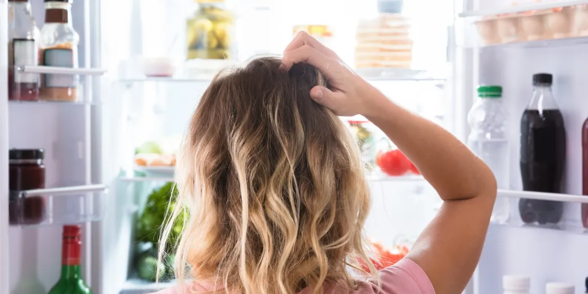 rear view of a confused woman looking in open refrigerator at home