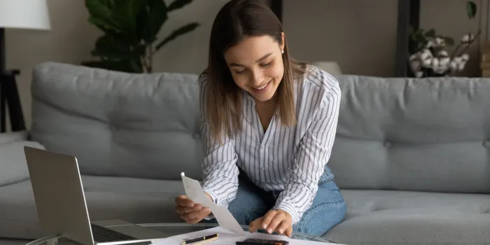 happy young woman holding paper bills in hands, calculating expenditures, paying bills or services online in computer application, feeling satisfied with enough money, investment payments concept