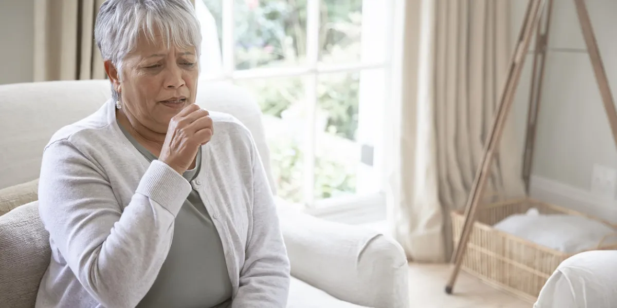 sick coughing senior woman with sore throat, sitting in living room at home
