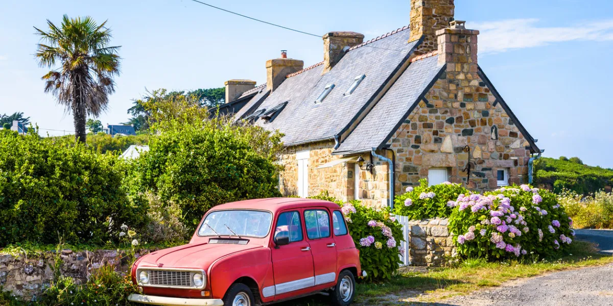 plougrescant, france - august 3, 2019  a renault 4 classic french car is parked in front of a typical granite house in brittany with slate roof, palm tree and hydrangea by a sunny summer day