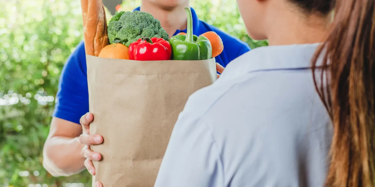 food delivery concept asian woman hand accepting bag of food, fruit, vegetable delivery from professional deliveryman postman and express grocery delivery