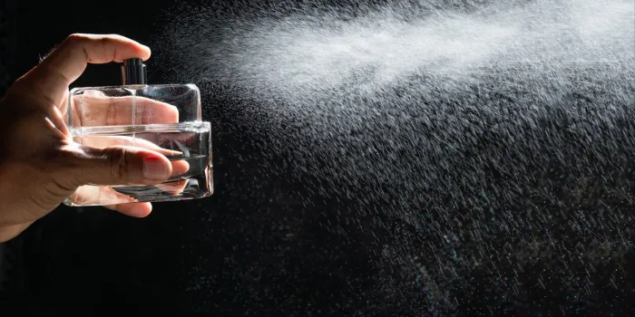 man spraying perfume on dark background, closeup