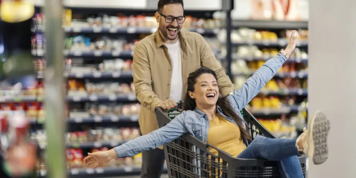 a man pushing shopping cart in supermarket in cart is his woman who is celebrating low prices