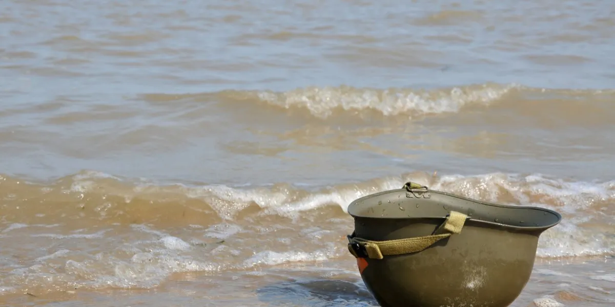 a lone ww2 us army helmet lies upside down on the normandy beach, a reminder never to forget the fallen