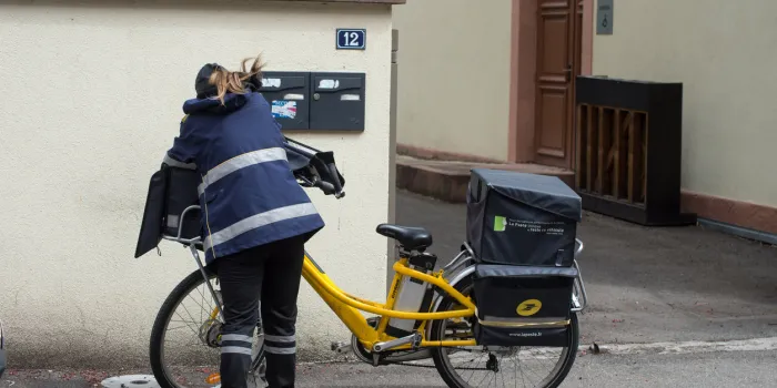 mulhouse - france - 4 may 2021 - portrait of postwoman putting letters in mail boxes in the street