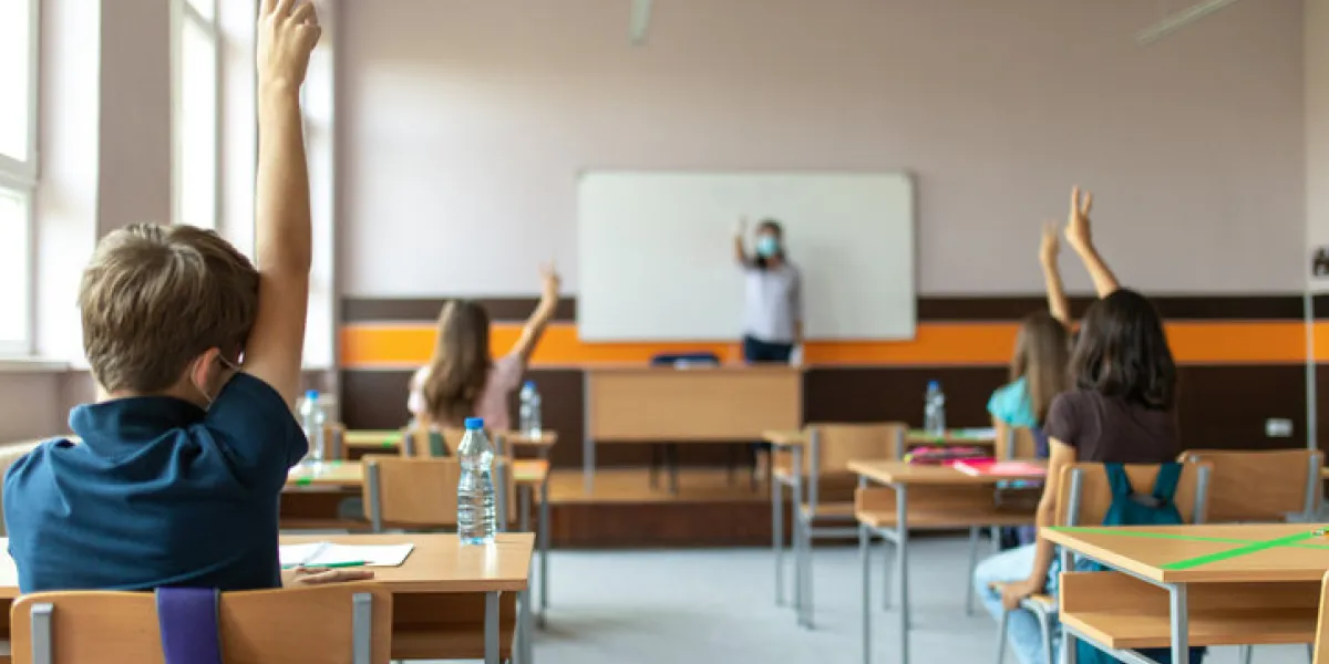 students with protective masks sitting in school desks in their classroom school desks are marked with a cross to mark a place where sitting is not allowed to maintain social distance during corona virus