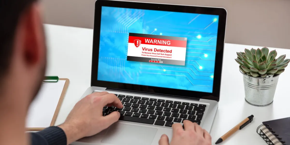 virus detected warning message on computer screen, cyber attack concept man working on a laptop, office business wood desk background