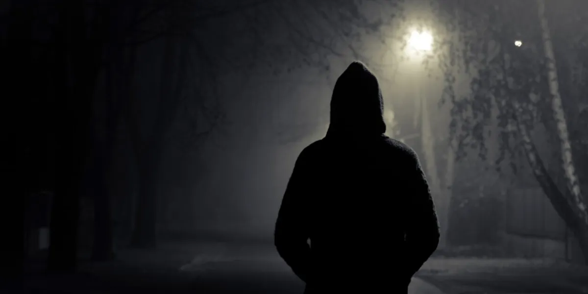 silhouette of hooded person with spooky dark background