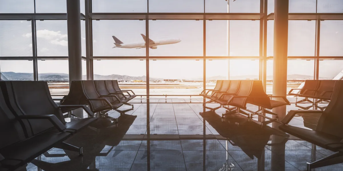 wide-angle view of a modern aircraft gaining the altitude outside the glass window facade of a contemporary waiting hall with multiple rows of seats and reflections indoors of an airport terminal el prat in barcelona