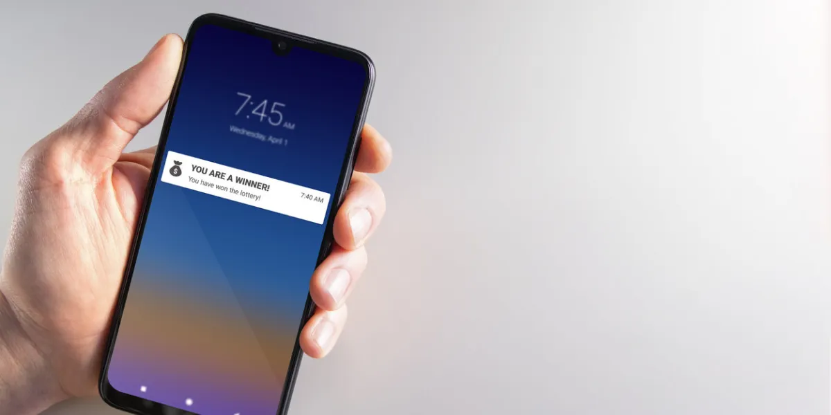 male hand holding a smartphone with lottery winner notification on april 1st scam, april fools, cybercrime, privacy and technology concepts