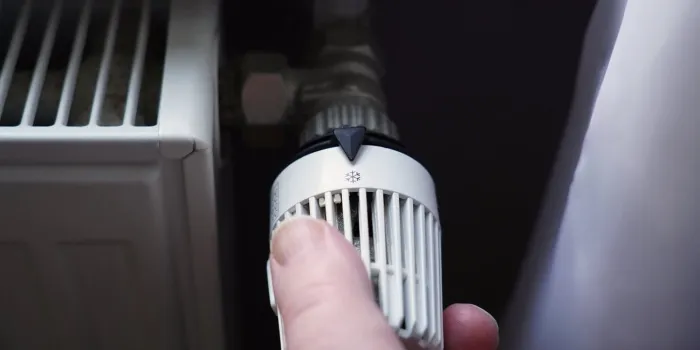 hand turning off thermostat on radiator to save energy due to increasing heating costs