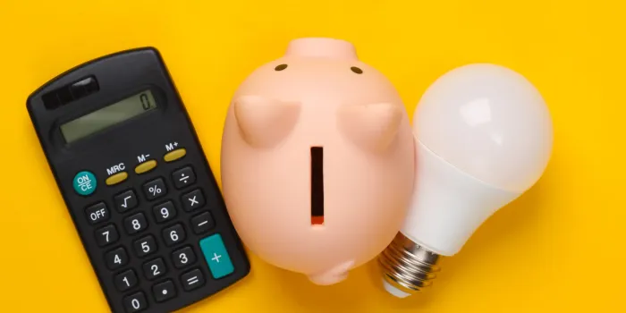 piggy bank and led light bulb, calculator on yellow background energy saving minimalistic studio shot overhead view flat lay