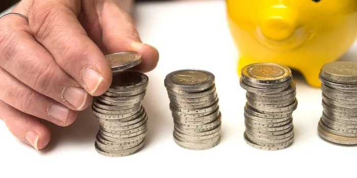 closeup of hand of woman stacking euro coins on a white table with a yellow piggy bank background