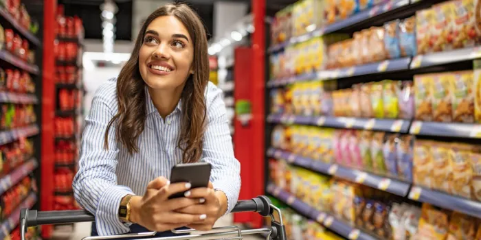 smiling woman at supermarket happy woman at supermarket beautiful young woman shopping in a grocery store supermarket shopping lists in app format