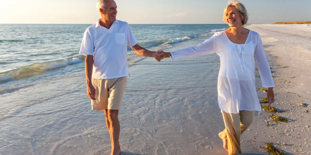 happy senior man and woman couple walking and holding hands on a deserted tropical beach with bright clear blue sky