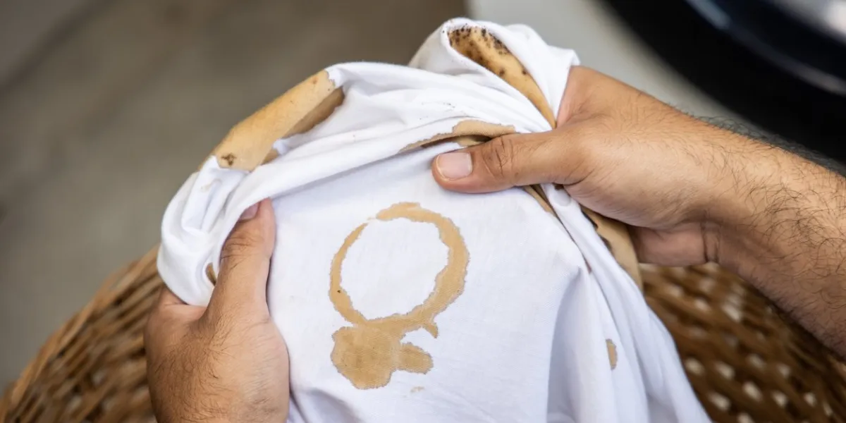 white cotton shirt a lot of stains, stains, coffee stains, man's hand holds the shirt up and spreads it to look dirty must be brought to the washing machine