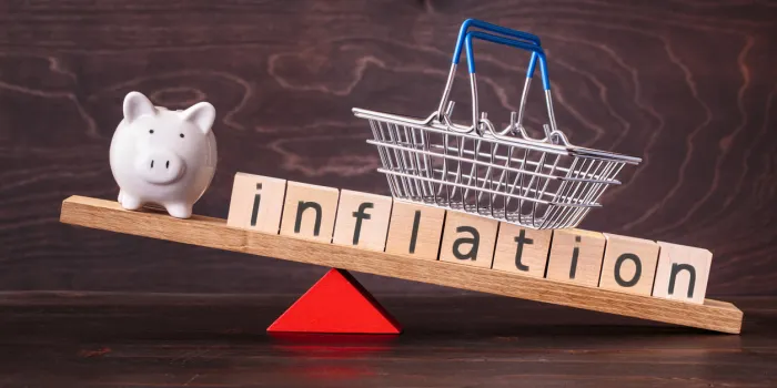 inflation spelled in letters with shopping basket and piggy bank on seesaw against dark background