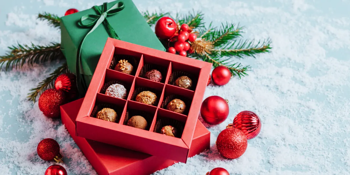 chocolates in a red festive box dark chocolate truffle on a christmas background with new year's toys balls fir branches top view flat mock up copy space holiday concept