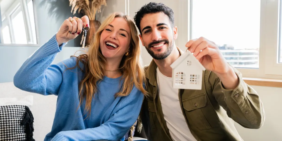 young adult couple looking at camera wife is holding the keys for the new apartment property boyfriend and girlfriend rent a house they are happy and smiling in the home interior high quality photo