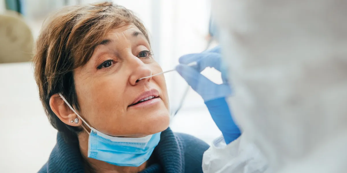 close up of the face of senior female patient being tested for covid-19 with a nasal swab, by a health professional protected with gloves and ppe suit rapid antigen test during coronavirus pandemic