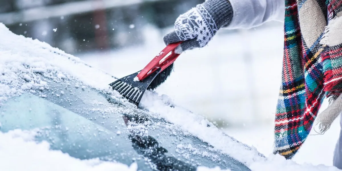 woman cleaning snow from windshield, scraping frozen ice glass