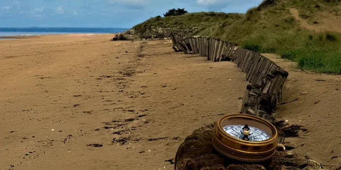 vintage brass compass on old post at utah beach in normandy region of france showing weathered wood fence, dunes with beach grass d-day world war 2 landing beaches