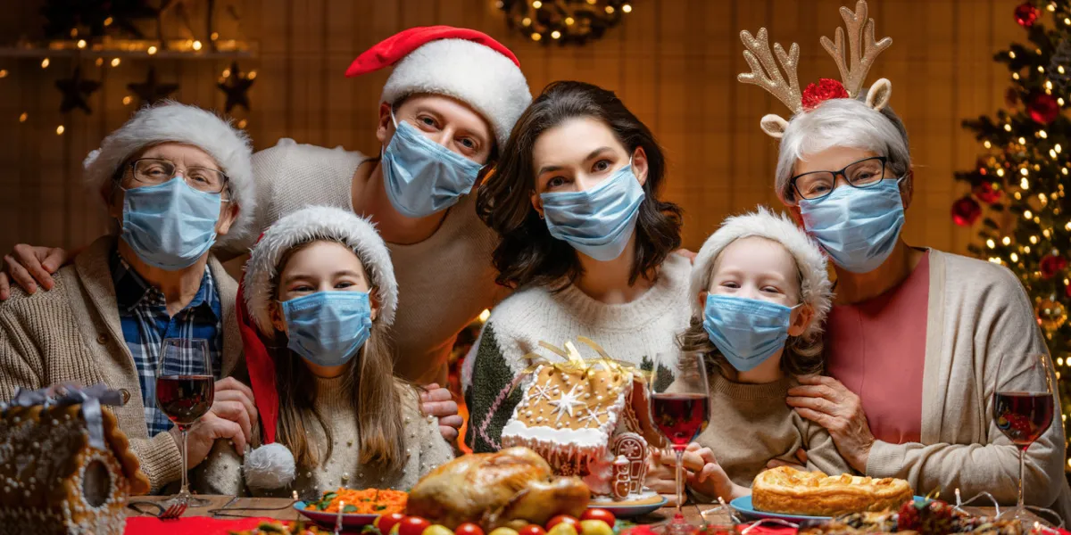 merry christmas happy family are having dinner at home celebration holiday and togetherness near tree people are wearing facemasks