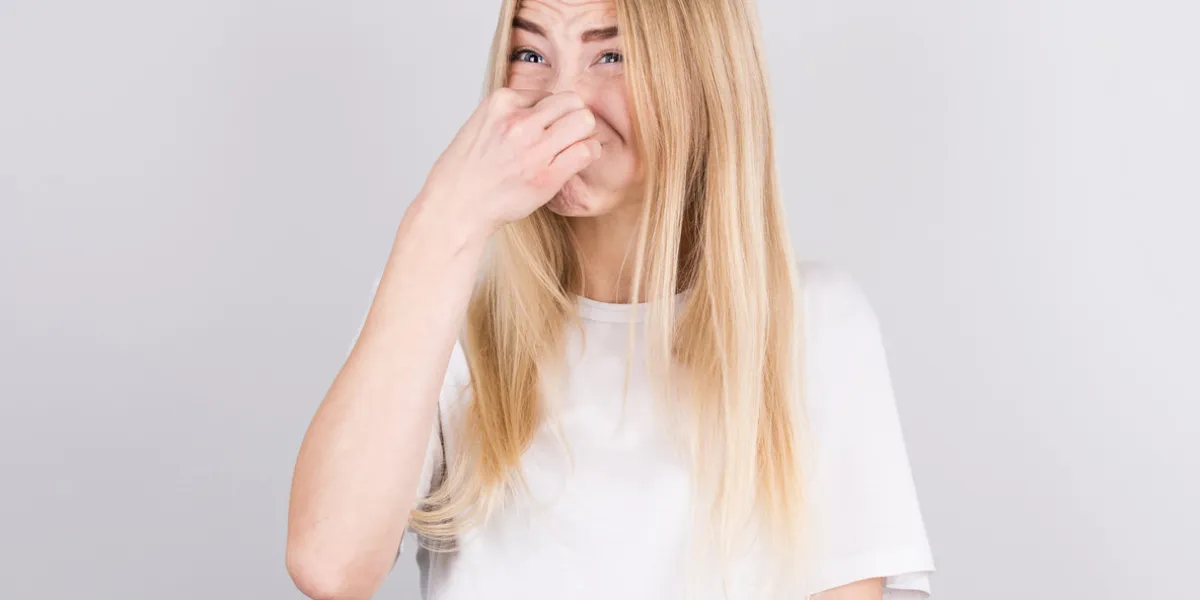 young woman with disgust on his face pinches nose on white background negative emotion facial expression