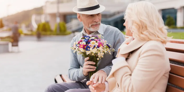 two pensioners are sitting on a bench in the alley an elderly man gives a woman flowers she is delighted with the gift