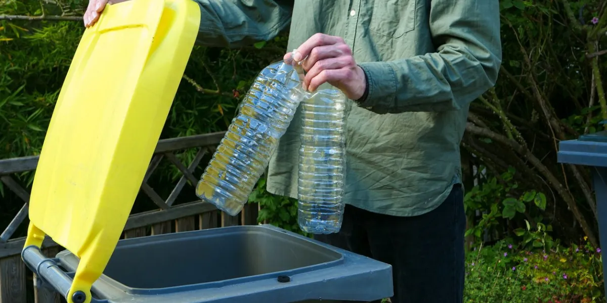 man putting plastic bottles in a yellow bin for recycling