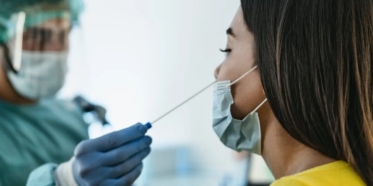 medical worker wearing personal protective equipment doing corona virus swab on female patient - covid19 test and health care concept