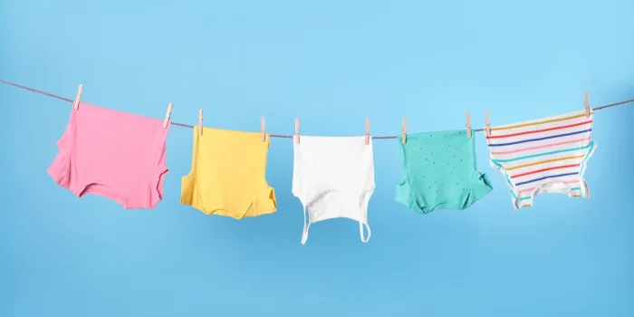 clean child's clothes hanging on laundry line against light blue background