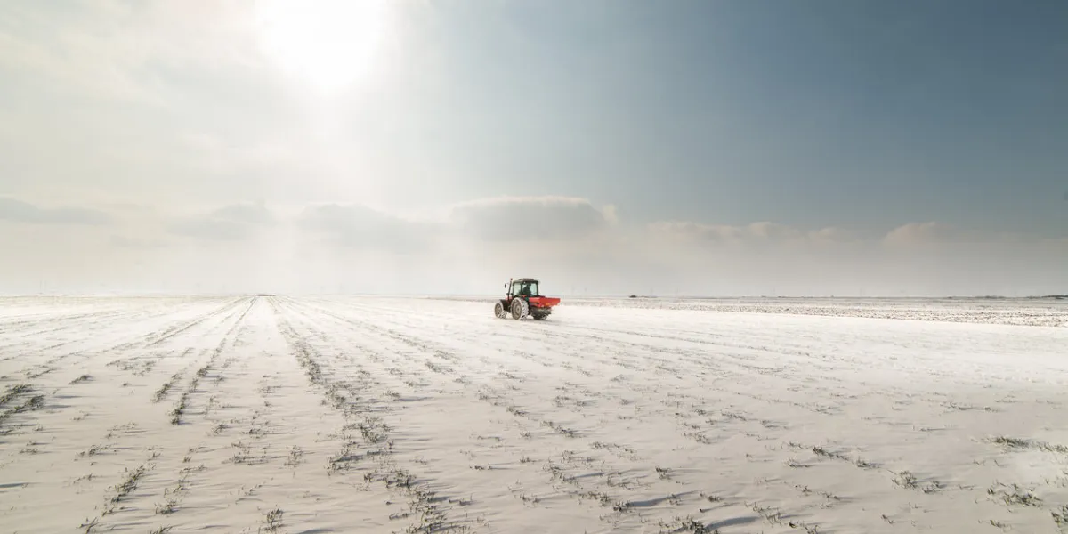 farmer with tractor seeding - sowing crops at agricultural fields in winter - snow