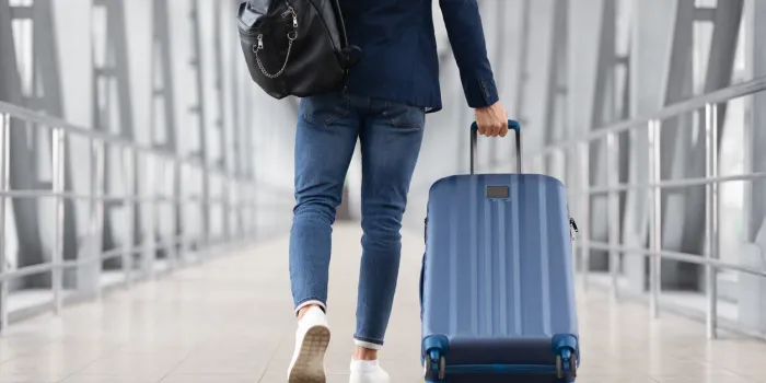unrecognizable man with bag and suitcase walking in airport terminal, rear view of young male on his way to flight boarding gate, ready for business travel or vacation journey, cropped, copy space