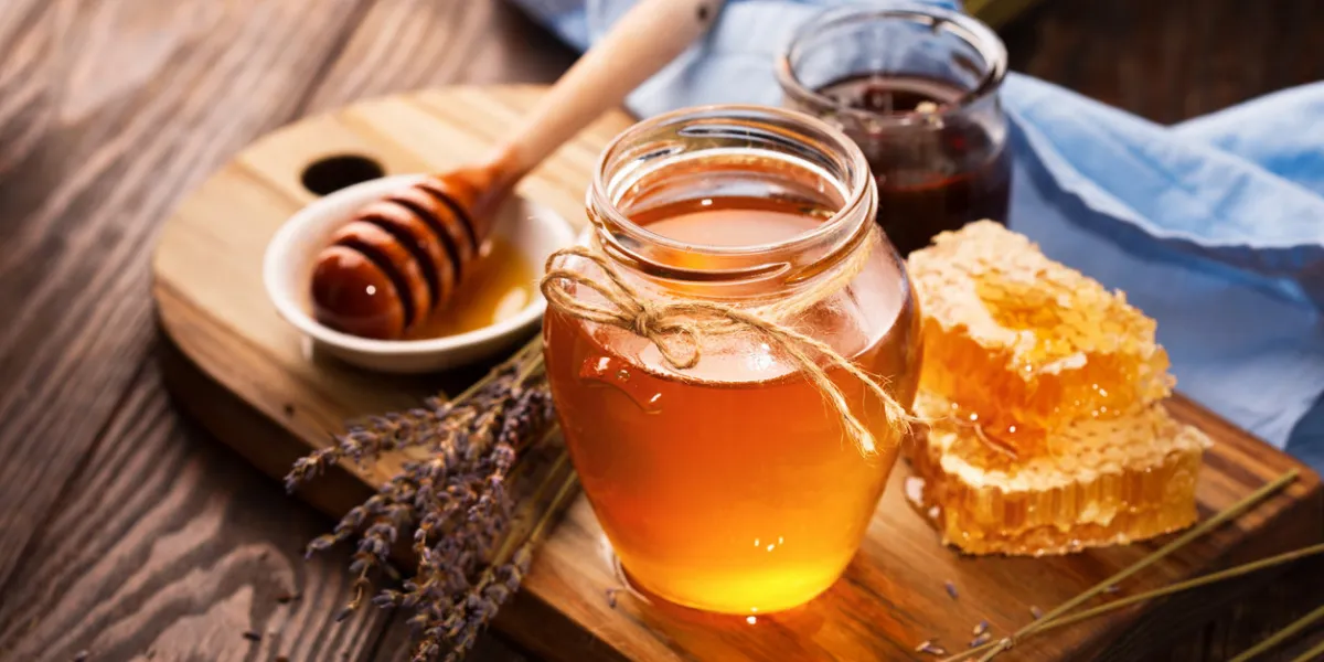 jar of liquid honey with honeycomb inside and bunch of dry lavender over old wooden table dark rustic style, selective focus