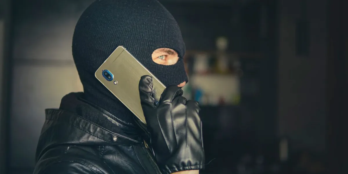 young adult in black clothes with hidden face ill-intended fraudster uses mobile fraudster calls scam mobile racket hacker hijacks by phone cellphone account fraud