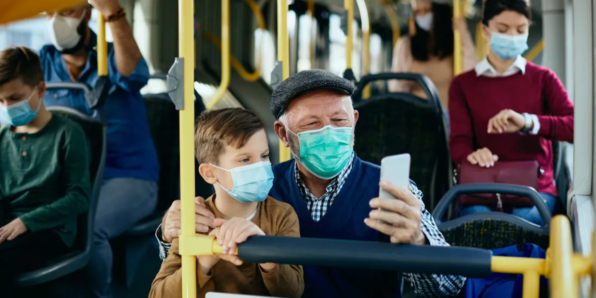 happy grandfather and grandson wearing protective face masks and taking selfie while commuting by bus