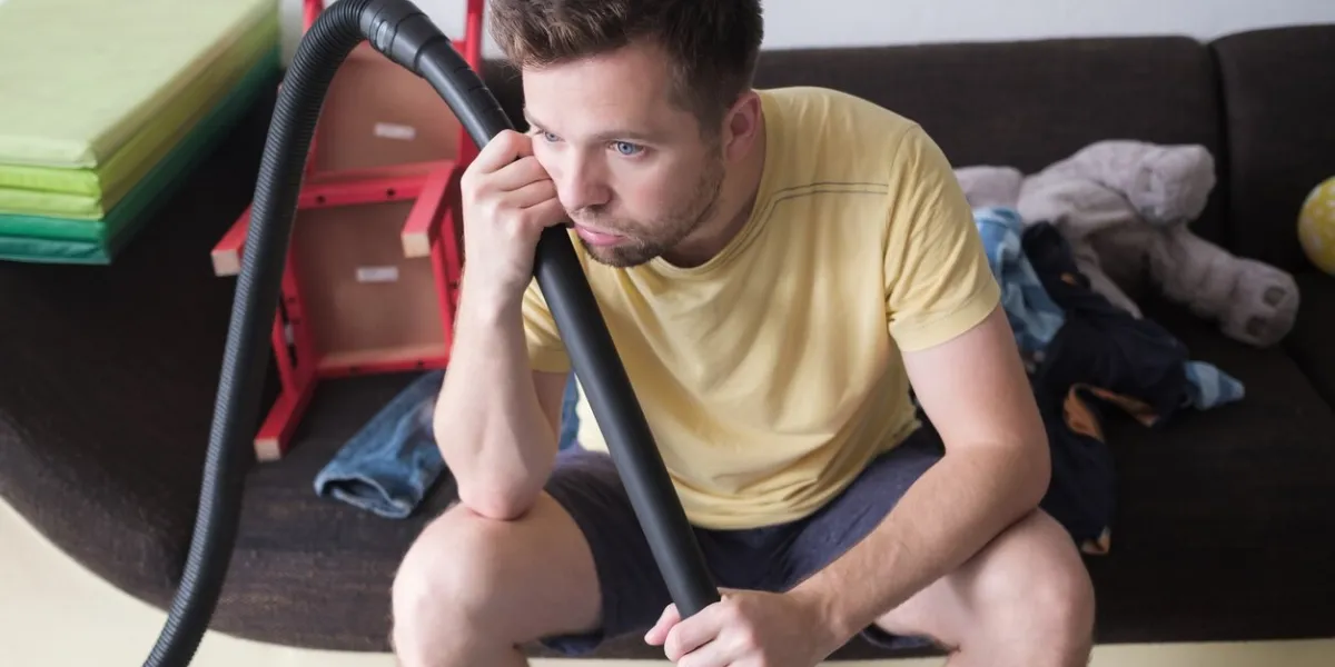 mature caucasian man sitting tired after cleaning floor with vacuum cleaner