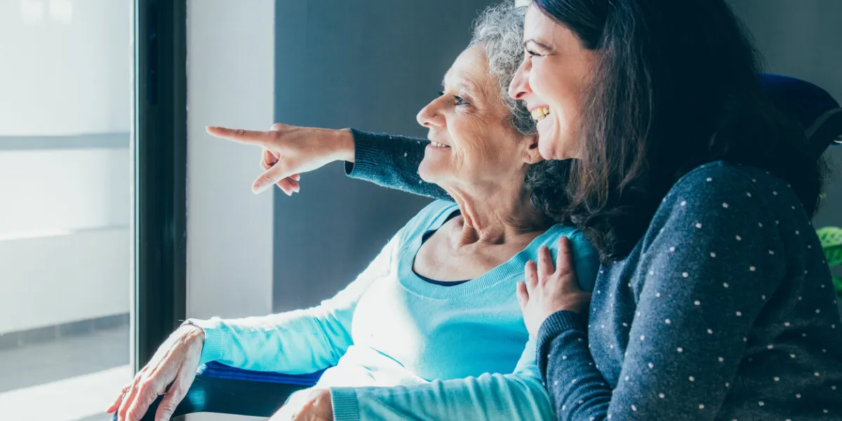 joyful woman taking care of elderly mother young woman hugging senior lady and showing something out of window positive emotions concept