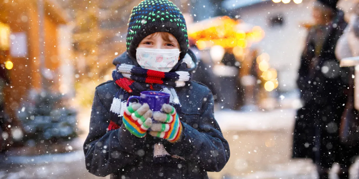 kid boy drinking hot children punch on german christmas market happy child with medical mask people with masks as protection against corona virus covid pandemic time in europe and in the world