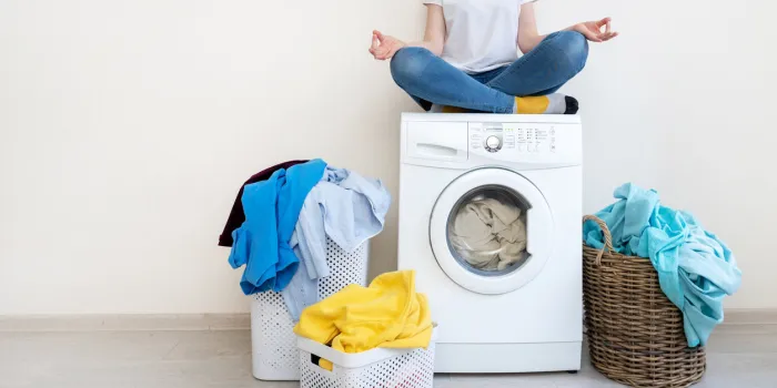 happy and recreation lady in denim jeans wear sitting near laundry basket inside bright light flat interior with copy space for text on top of washing machine in meditation pose
